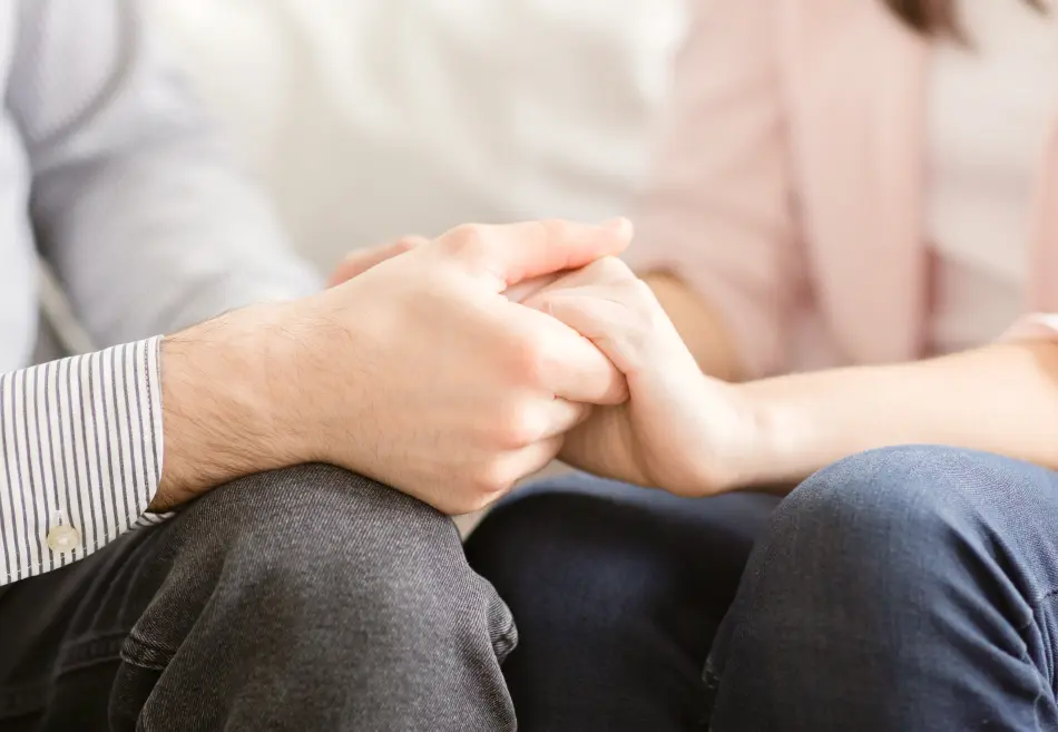 A close up shot of two people holding hands sitting on the couch