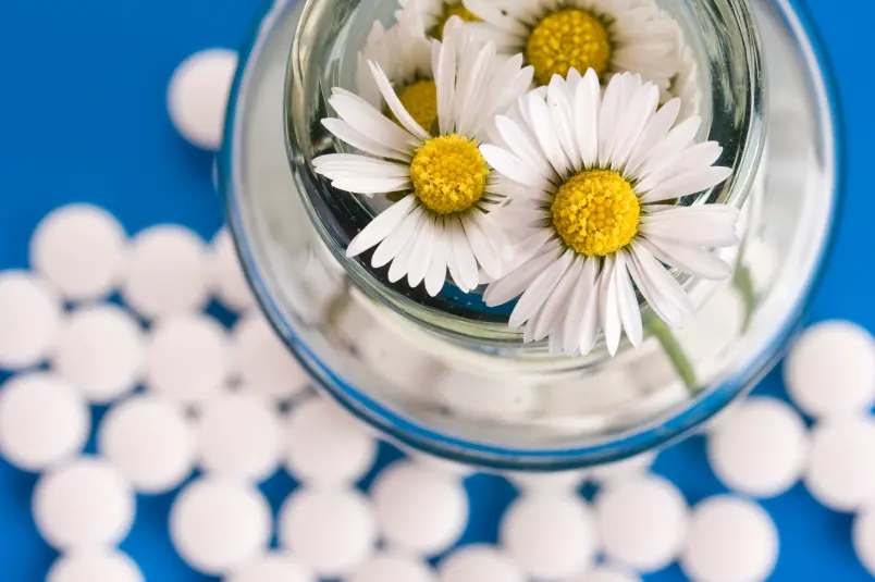 Pills on a blue backdrop with a jar of daisies