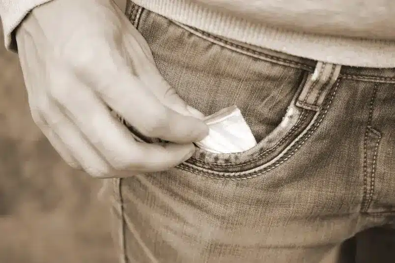 A teenage boy puts a packet of powdered substance into his jean pocket
