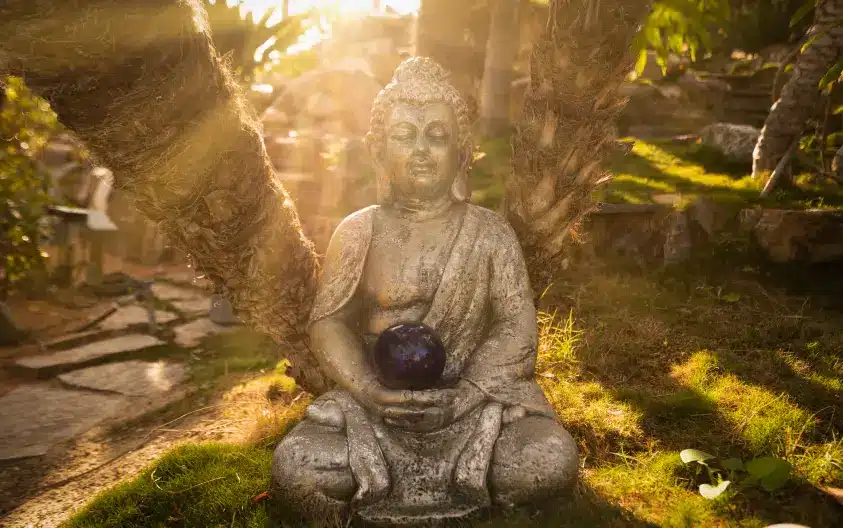 A shot of our statue of Buddha. Sunlight is peeking through the trees behind the statue, giving it a warm glow