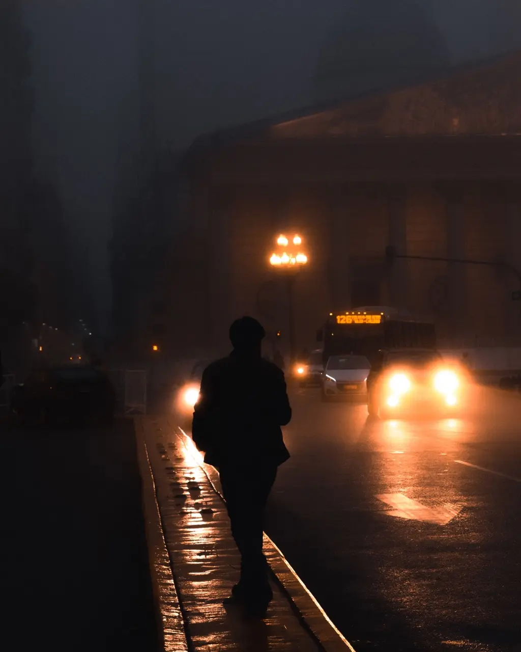 A person walking along a wet street at night