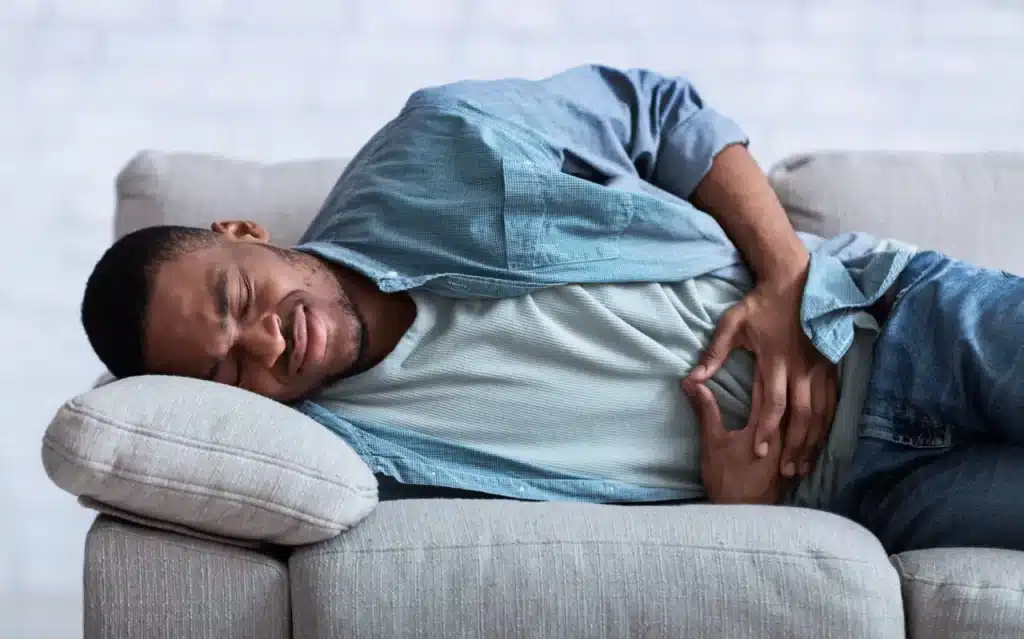 African guy suffering from a stomach ache from alcohol detox at Villa Oasis San Diego laying on his side on the couch while holding his stomach