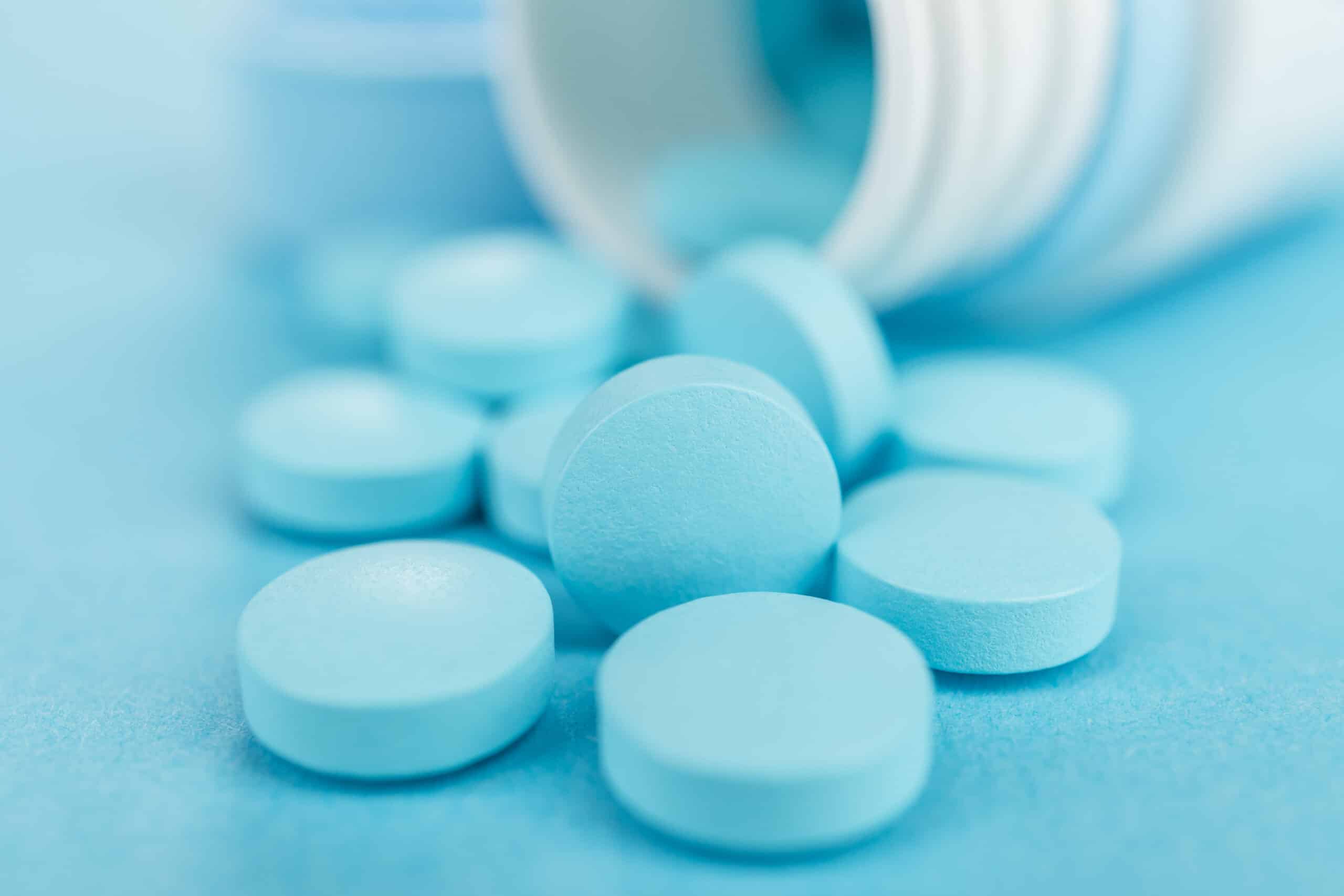 overturned plastic jar with pills on blue background