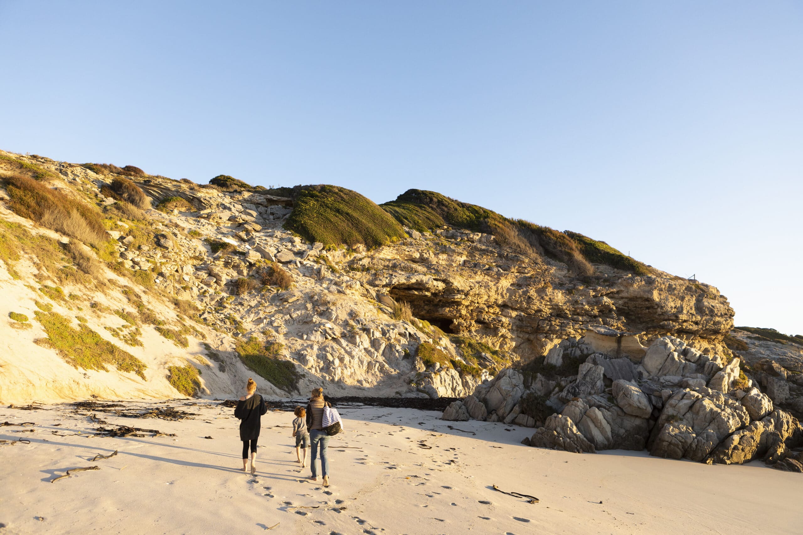 A family walking along a sandy beach towards the cliffs.