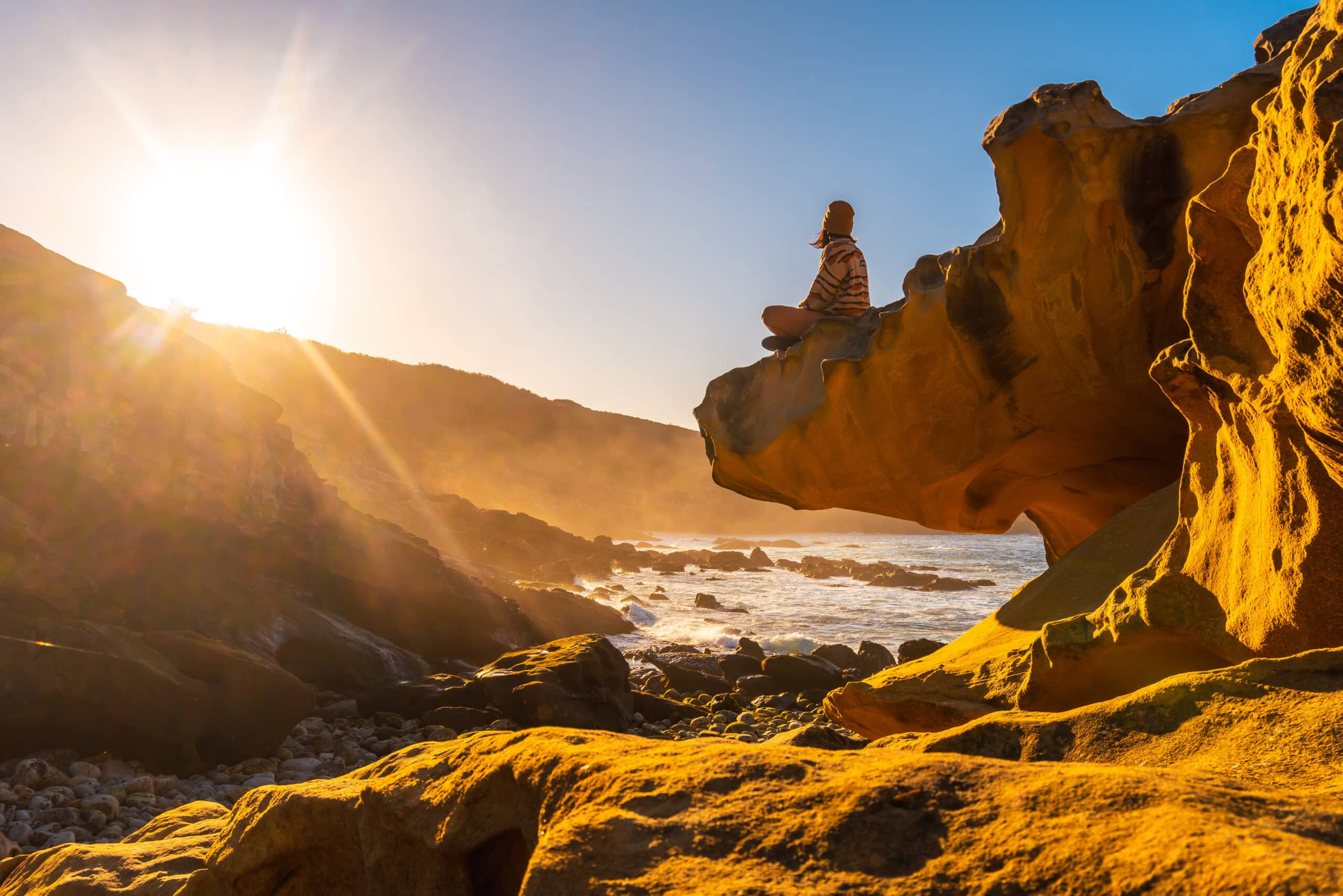 A young woman relaxed at sunset in the cove of stones in the Jaizkibel mountain in the town of Pasajes, Gipuzkoa. Basque Country