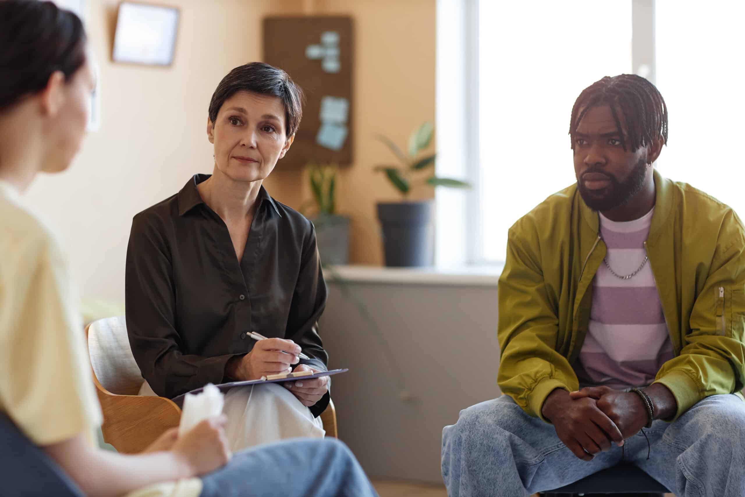 Mature psychologist working with group of people at psycho session in office