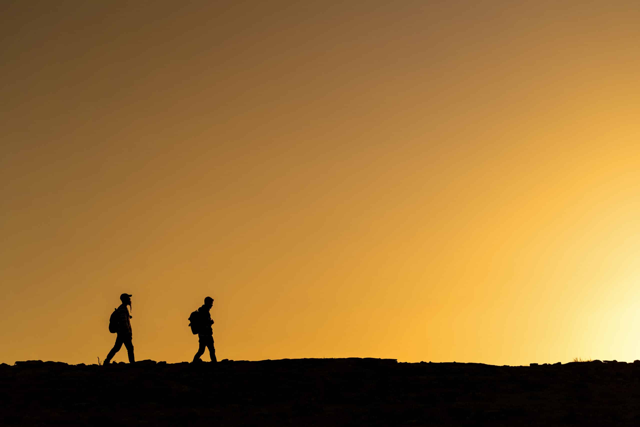 People silhouettes walking over mountain at colorful sunset. Hiking concept