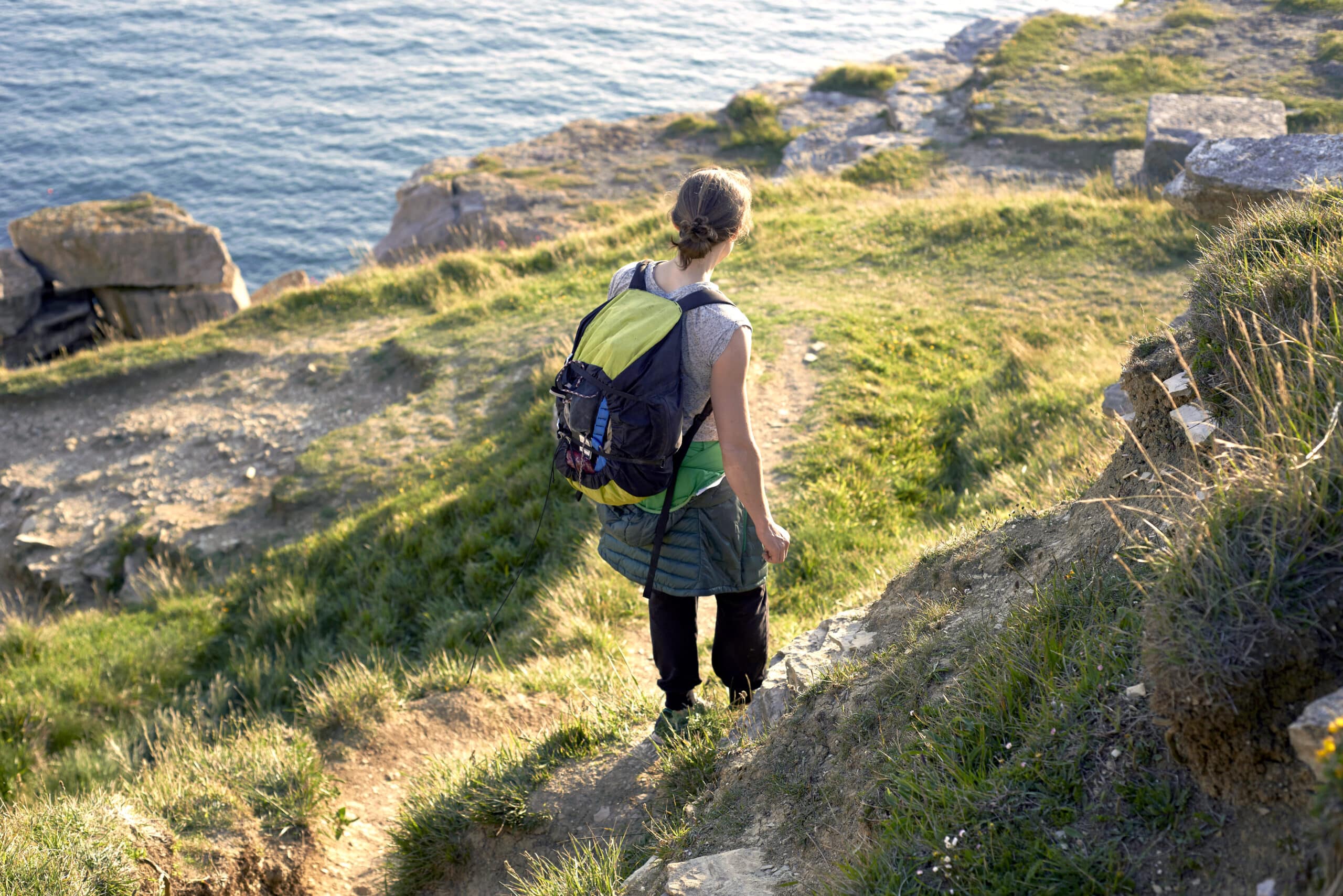 High angle rear view of hiker with backpack hiking down cliff side, Portland, UK