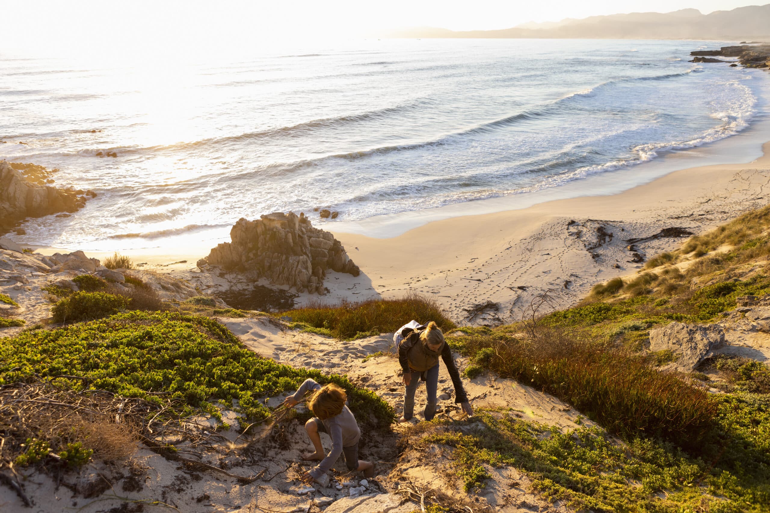 Young boy and mature woman climbing up a cliff path at sunset.